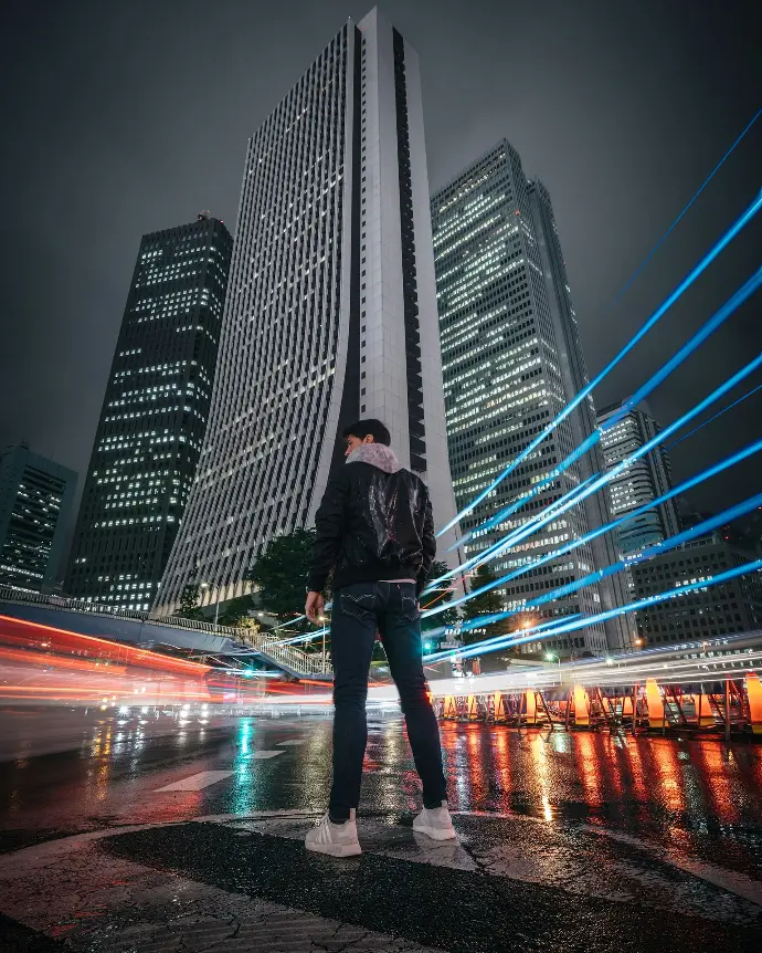 man in black jacket and blue denim jeans standing on road during night time